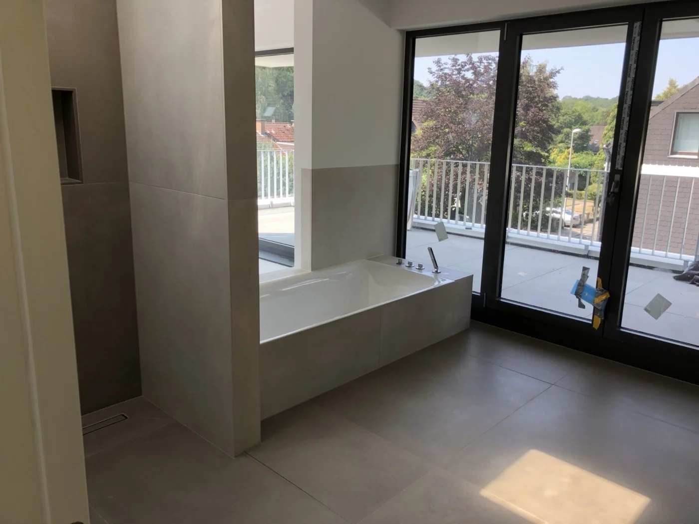 Helles Badezimmer mit freistehender Badewanne vor bodentiefen Fenstern mit Blick auf die Terrasse