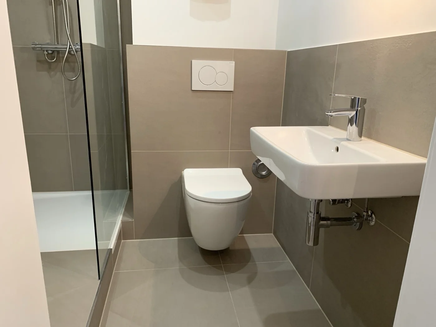 Minimalistisches Badezimmer mit großformatigen grauen Fliesen, Glasdusche und wandhängendem WC