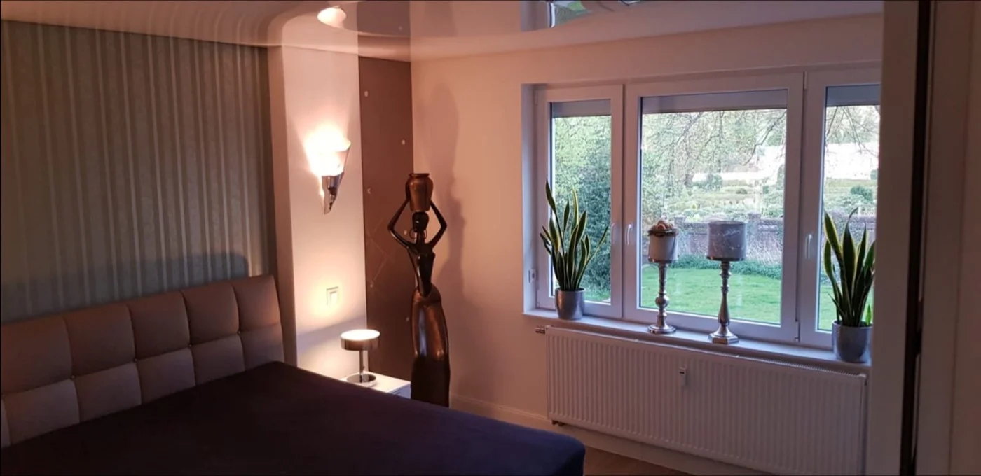 Gemütliches Wohnzimmer mit großen Fenstertüren, Blick in den Garten und stimmungsvoller Beleuchtung